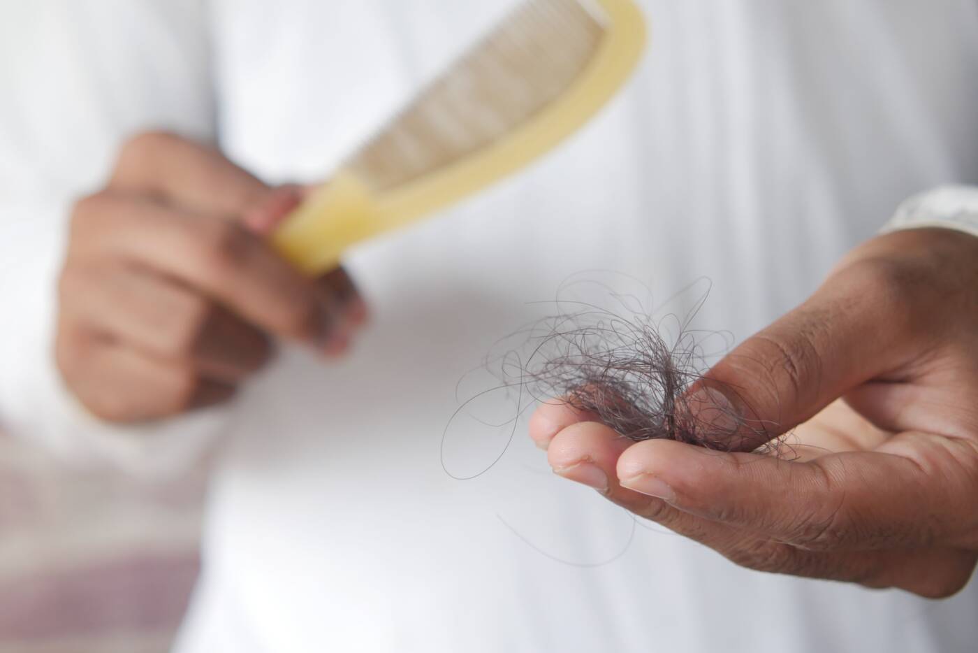Mão segurando fios de cabelo próximos a uma escova, ilustrando queda e quebra capilar