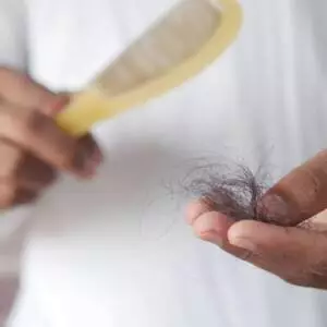 Mão segurando fios de cabelo próximos a uma escova, ilustrando queda e quebra capilar