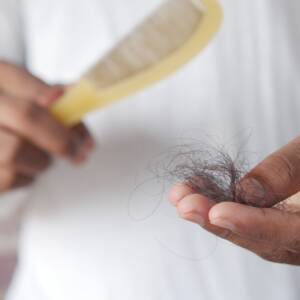 Mão segurando fios de cabelo próximos a uma escova, ilustrando queda e quebra capilar